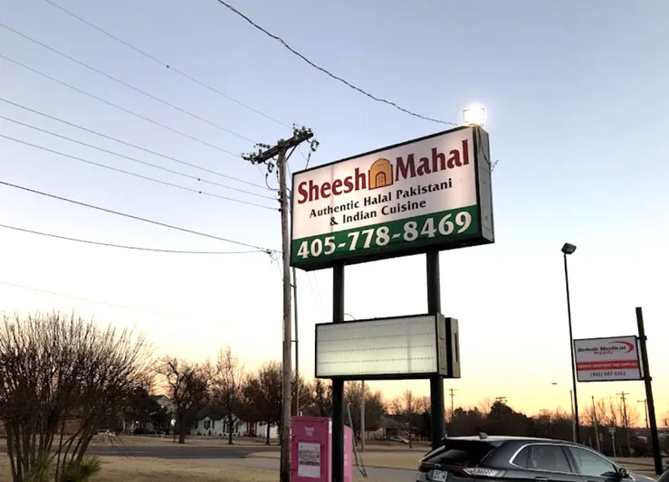 Roadside sign for Sheesh Mahal reading 'Authentic Halal Pakistani & Indian Cuisine' with the phone number 405-778-8469, on N May Ave in Oklahoma City