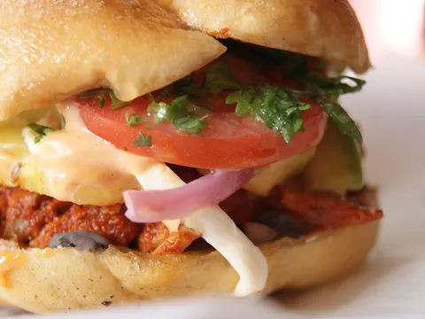 Close-up of a Mexican torta on a telera roll with al pastor pork, melted cheese, tomato, red onion, avocado and cilantro at Tenoch Mexican in Medford