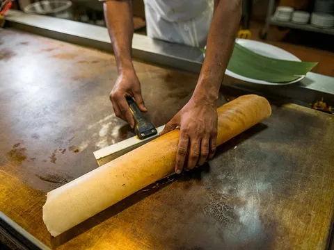 A cook rolling a large dosa on the griddle at Madras Mantra in Decatur.