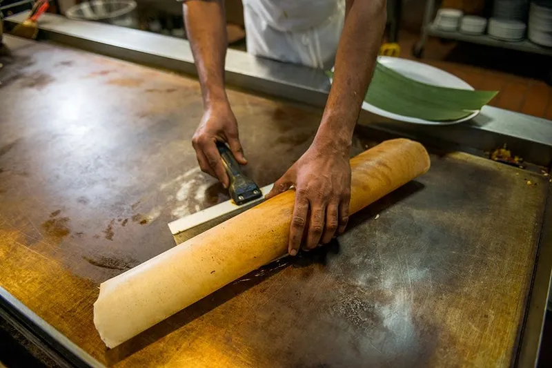 A cook rolling a large dosa on the griddle at Madras Mantra in Decatur.