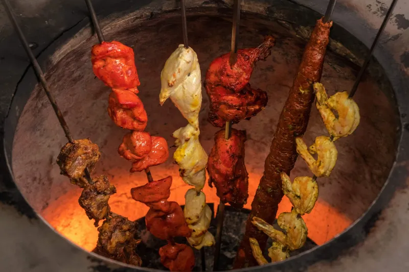 Assorted tandoori kebabs, chicken and shrimp on skewers cooking inside the glowing tandoor oven at Chola in New York