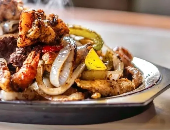 A sizzling cast-iron skillet of mixed shrimp, beef and chicken fajitas with grilled onions and peppers at Los Asaderos in Fort Worth