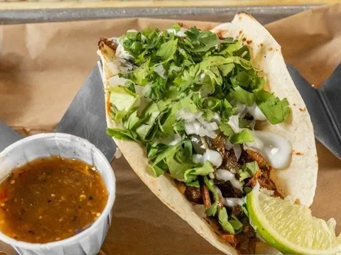 A suadero taco on a flour tortilla topped with cilantro, onion and crema with a lime wedge and a cup of salsa verde, from KC Taco Company in Kansas City