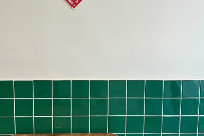 Interior corner at Ho Foods in New York — a wooden table against a green-tiled wall with a red paper-cut good-fortune decoration and a teal stool
