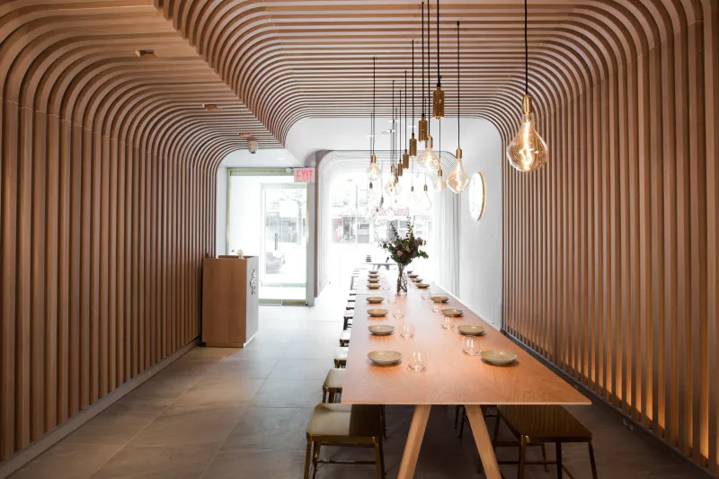 Hunan Slurp's wood-slatted dining room with a long communal table and hanging Edison-bulb pendants