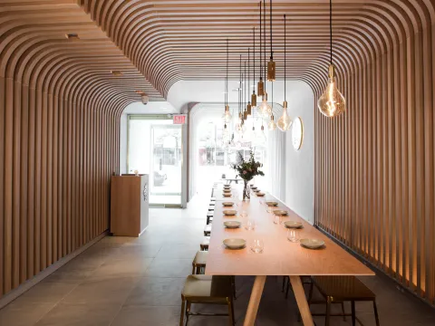 Hunan Slurp's wood-slatted dining room with a long communal table and hanging Edison-bulb pendants