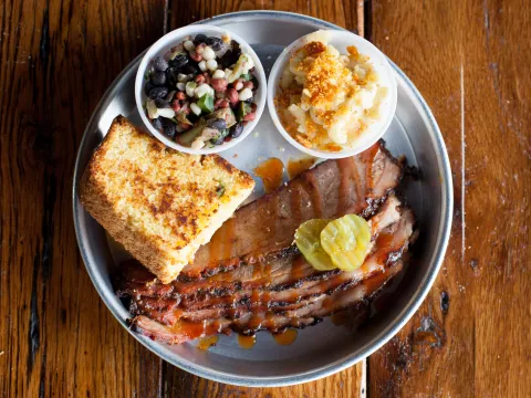 Edley's Bar-B-Que sliced brisket platter with grilled cornbread, mac and cheese, bean salad and pickles on a metal plate