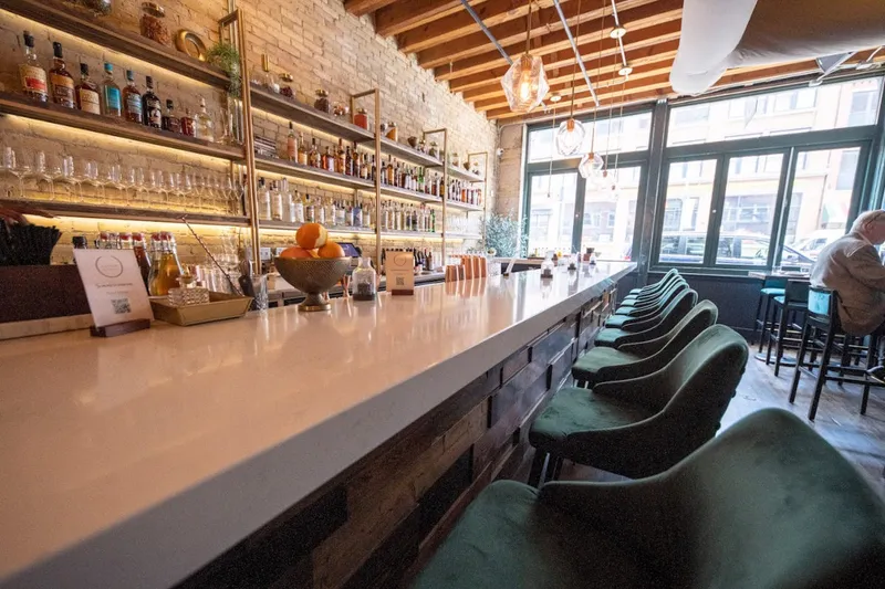 Long bar with green stools and a lit back bar at Saffron in Milwaukee's Third Ward