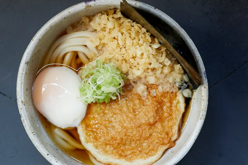 Bowl of Rintaro's hand-rolled kake/kama-tama udon topped with a soft egg, grated daikon, tenkasu and scallion, from the Rintaro website