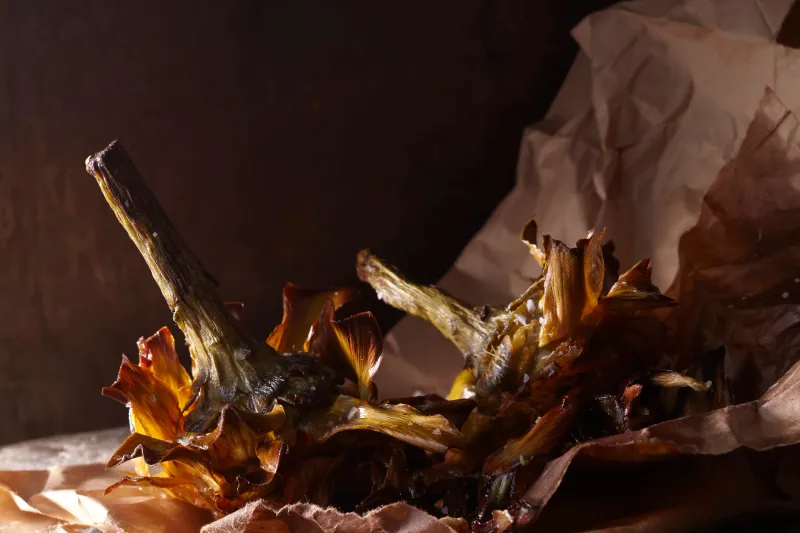 Grilled artichokes served on brown parchment paper at Via Carota