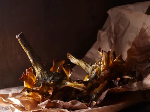 Grilled artichokes served on brown parchment paper at Via Carota