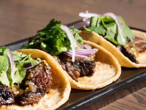 Three grilled steak tacos topped with cilantro and pickled red onion on a black plate at La Josie