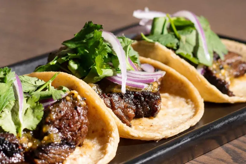 Three grilled steak tacos topped with cilantro and pickled red onion on a black plate at La Josie