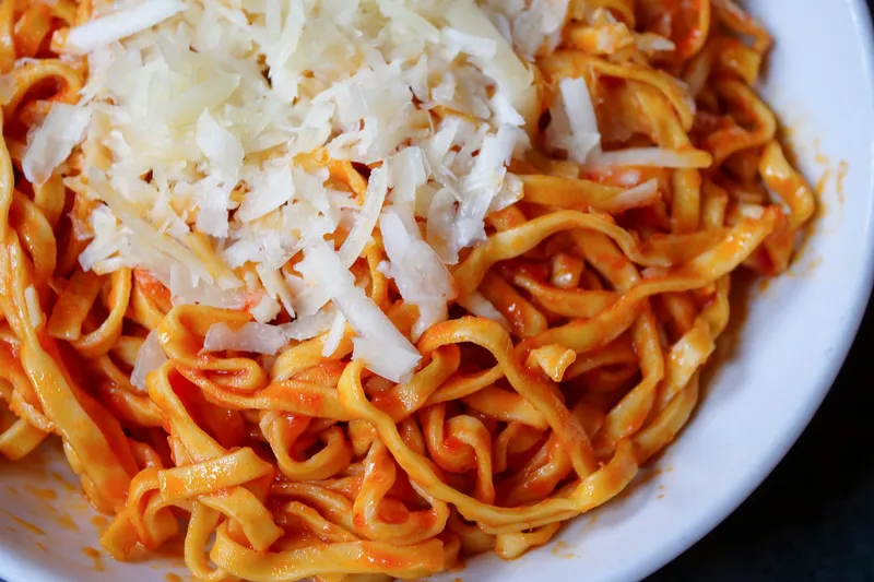 A bowl of Pastabilities' signature spicy hot tomato oil pasta topped with shredded locatelli cheese