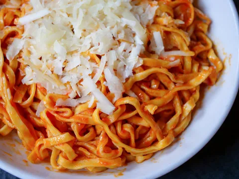 A bowl of Pastabilities' signature spicy hot tomato oil pasta topped with shredded locatelli cheese