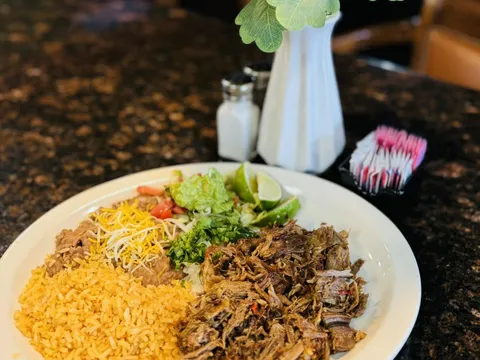 Carnitas plate with Mexican rice, refried beans topped with cheese, guacamole, pico de gallo and lime at Tacos El Charrito in Denver