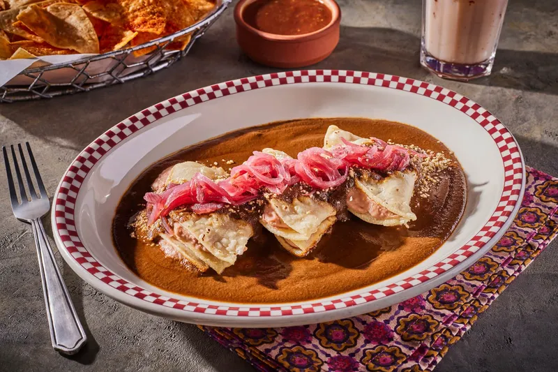 A plate of enmoladas topped with pickled red onions in dark mole sauce at Red Iguana