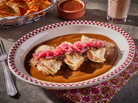 A plate of enmoladas topped with pickled red onions in dark mole sauce at Red Iguana