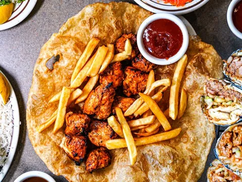 Overhead spread of grilled chicken boti and fries on fried flatbread with chutneys, mango lassi and rice at Bundu Khan