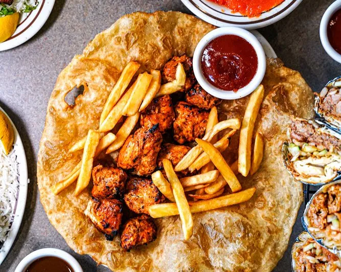Overhead spread of grilled chicken boti and fries on fried flatbread with chutneys, mango lassi and rice at Bundu Khan