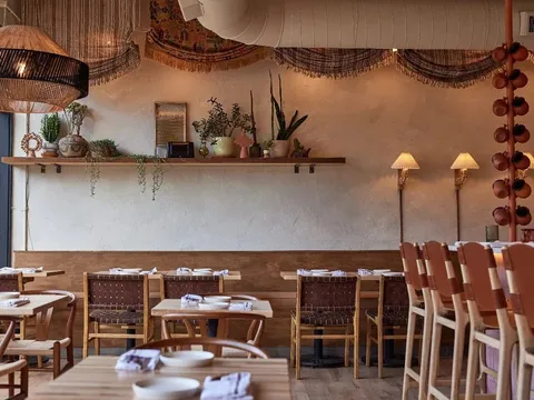 The plaster-walled dining room at Alma Fonda Fina in Denver, with woven-leather chairs, banquette seating and hanging terracotta cups along the bar