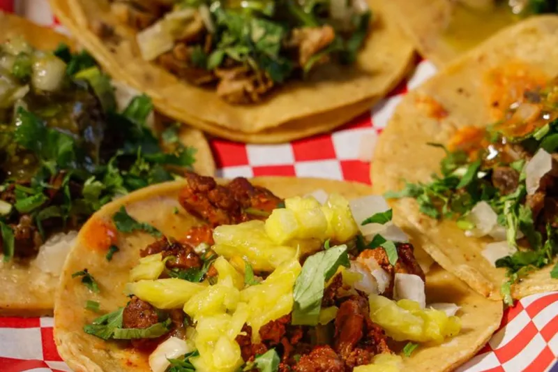 Jalisco Taqueria's al pastor and asada street tacos on corn tortillas with cilantro, onion and pineapple, served in a red-checkered paper basket