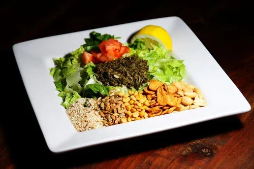 Tea leaf salad at Burma Superstar arranged on a white plate with fermented tea leaves, tomatoes, lettuce, fried garlic, peanuts and sesame seeds