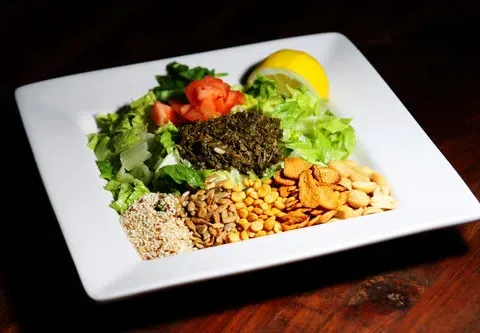 Tea leaf salad at Burma Superstar arranged on a white plate with fermented tea leaves, tomatoes, lettuce, fried garlic, peanuts and sesame seeds
