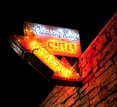 The illuminated neon 'Pleasant Ridge Chili Restaurant' storefront sign lit up at night on the corner of the stone building