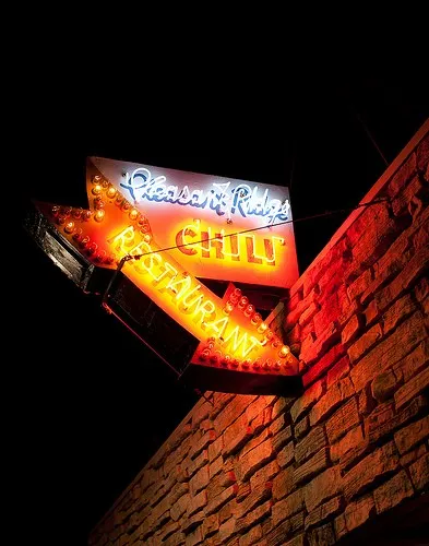 The illuminated neon 'Pleasant Ridge Chili Restaurant' storefront sign lit up at night on the corner of the stone building