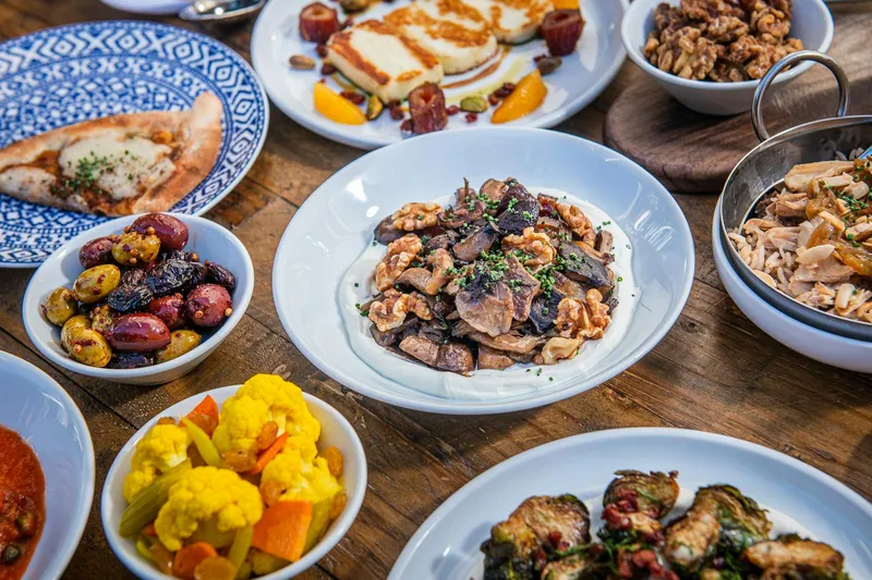 Spread of Zaytinya mezze including mushroom kapnistá, seared halloumi, olives, pickled cauliflower, charred eggplant pide and crispy brussels afelia on a wood table, Washington DC