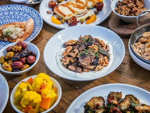 Spread of Zaytinya mezze including mushroom kapnistá, seared halloumi, olives, pickled cauliflower, charred eggplant pide and crispy brussels afelia on a wood table, Washington DC