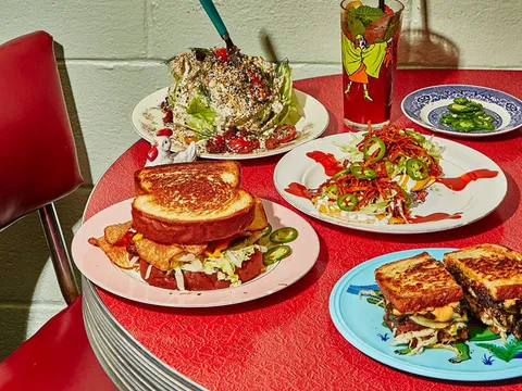 A spread of Turkey and the Wolf dishes — a wedge salad, fried bologna sandwich, loaded fries, and a cocktail — on a red diner table