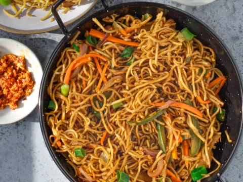 Wok of vegetable Hakka noodles with carrots, bell peppers and scallions, served with a side of noodles and chili garlic sauce, at Hakka Express in Austin