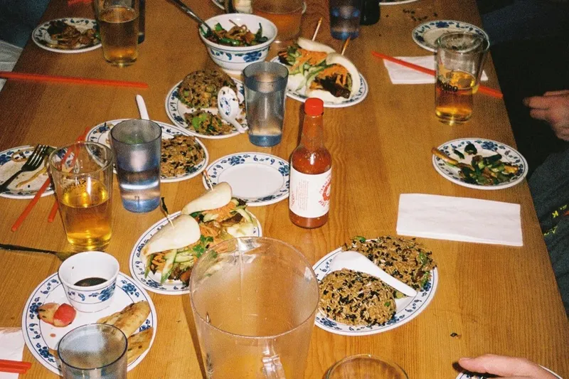 Woon dishes including noodles, fried rice, bao, chicken wings, and pickled vegetables spread across a dining table