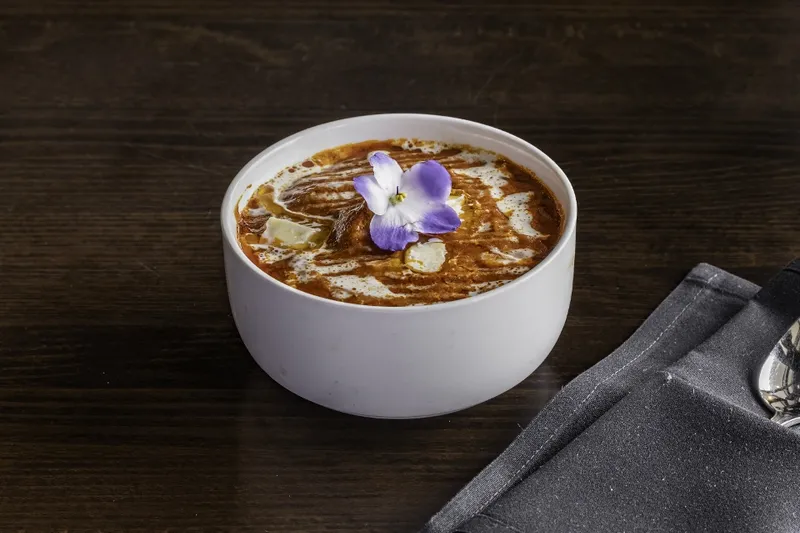 Butter chicken curry with a cream swirl and edible flower garnish, served at Artha - The Indian Bistro in Kirkland