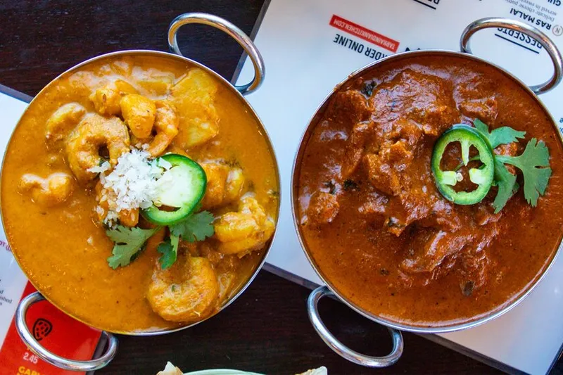 Four Indian curries in metal serving bowls arranged across a restaurant table