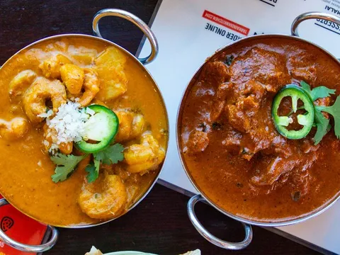 Four Indian curries in metal serving bowls arranged across a restaurant table