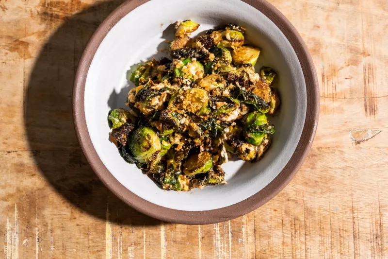 Overhead bowl of Paadee's sauteed fried brussels sprouts with egg and garlic on a wood table