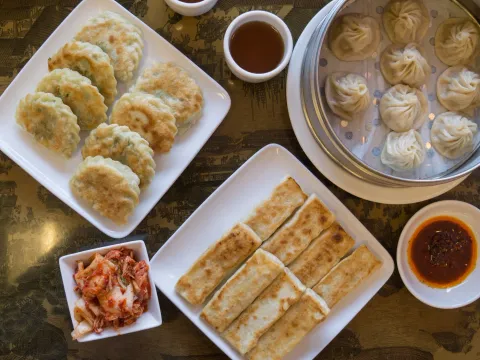 A spread of pan-fried hui tou dumplings, a steamer of xiao long bao, pan-fried scallion pancake, kimchi and chili oil at Hui Tou Xiang