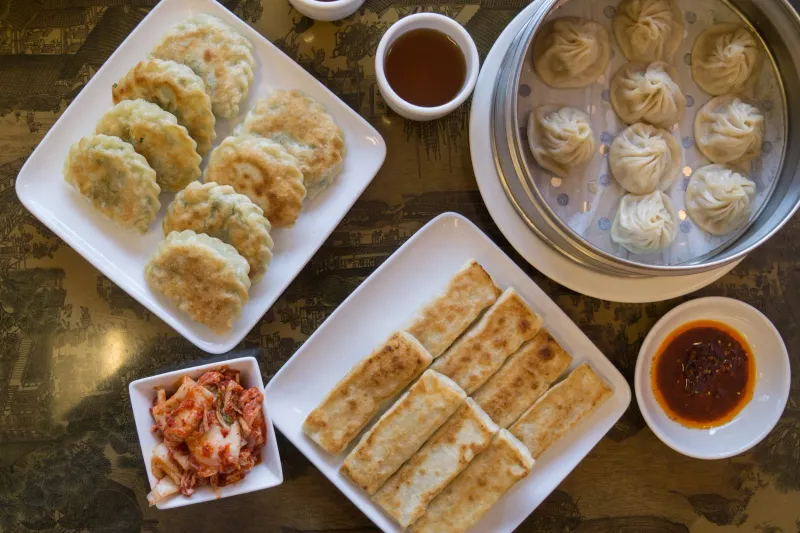 A spread of pan-fried hui tou dumplings, a steamer of xiao long bao, pan-fried scallion pancake, kimchi and chili oil at Hui Tou Xiang