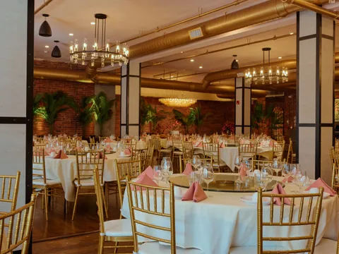 China Pearl's chandelier-lit banquet dining hall in Boston Chinatown, with round tables in white linens, gold Chiavari chairs, pink napkins, and exposed-brick walls
