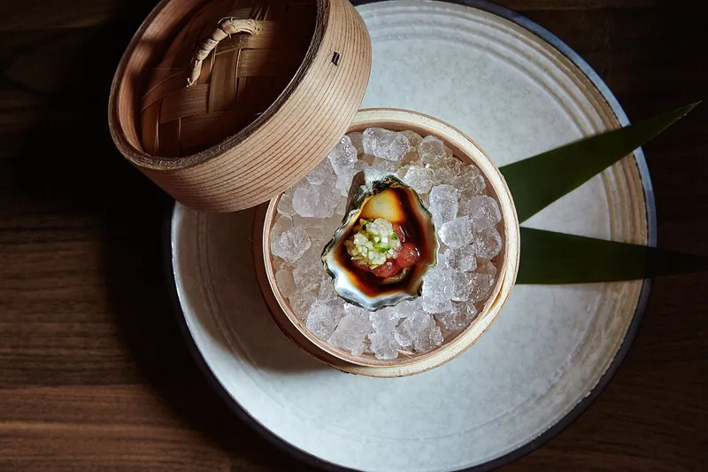 Overhead view of an O Ya dish in Boston: a single oyster with ponzu and relish served on crushed ice in a wooden vessel