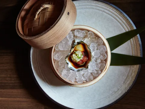Overhead view of an O Ya dish in Boston: a single oyster with ponzu and relish served on crushed ice in a wooden vessel