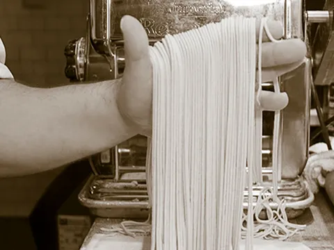 Fresh pasta sheets passing through a metal pasta roller at Lucia
