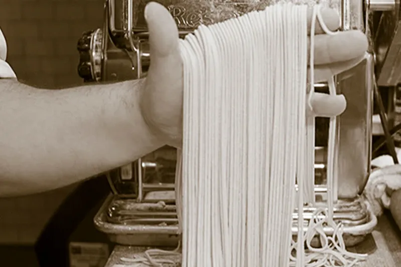 Fresh pasta sheets passing through a metal pasta roller at Lucia