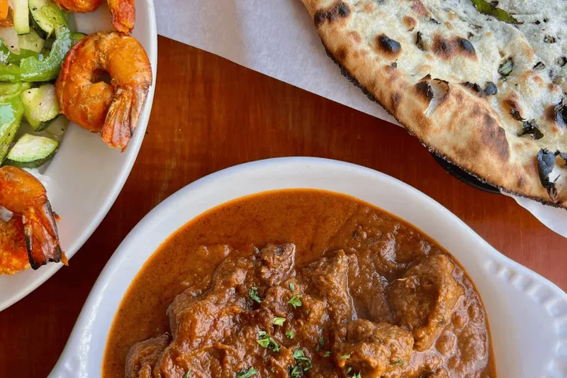 A dish of curry with a plate of tandoori shrimp, grilled vegetables and charred naan at Cedars in University District