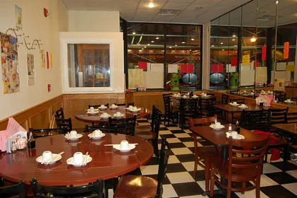 Interior dining room at Great Taste Bakery & Restaurant in Boston Chinatown, with round and square tables set with teapots and cups over a black-and-white checkered floor
