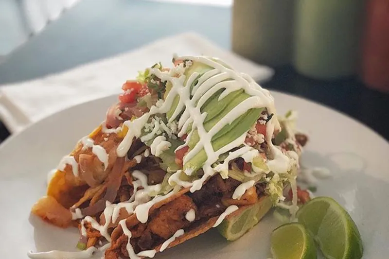 A plate of Maciel's fried tacos topped with sliced avocado, crema, pico de gallo and lime wedges