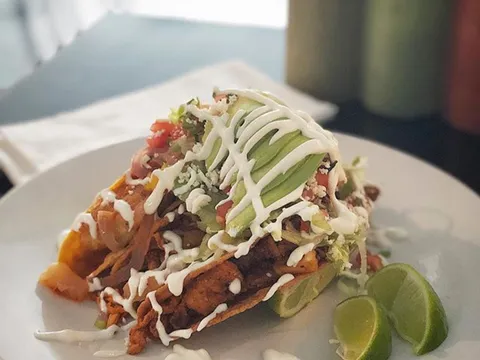 A plate of Maciel's fried tacos topped with sliced avocado, crema, pico de gallo and lime wedges